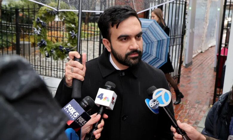 Zohran Mamdani speaks to reporters while holding an umbrella in the rain.