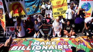 People protesting with signs and banners reading "Cut Billionaires Free New York," "No Troops No War Noice," "Defend Earth," and "Make Billionaires Pay."