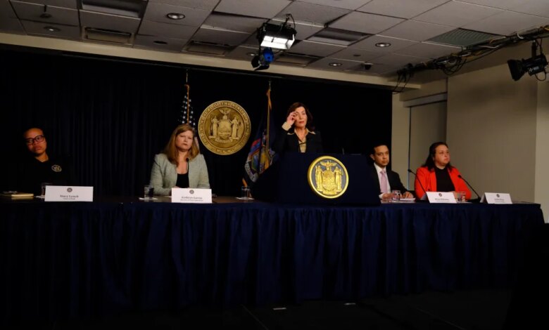 Governor Kathy Hochul speaking at a podium with Stacy Lynch, Kathryn Garcia, Brian Mahanna, and Jackie Bray seated at a table.