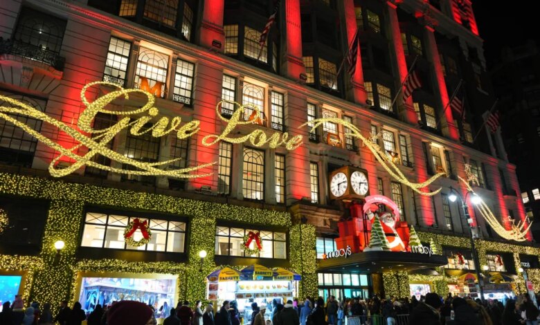 Black Friday shoppers gather outside Macy's in Herald Square, lit up with holiday decorations including a "Give Love" sign.