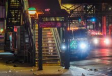 The entrance to West Farms Square-East Tremont Avenue train station at night, with an NYPD police truck and other emergency vehicles with flashing lights on the street in the background.