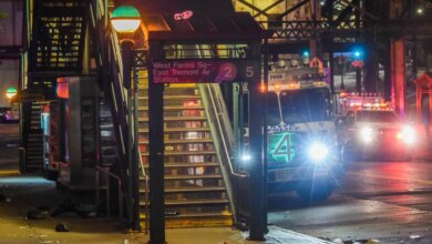 The entrance to West Farms Square-East Tremont Avenue train station at night, with an NYPD police truck and other emergency vehicles with flashing lights on the street in the background.