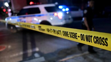 Police car with flashing lights behind yellow crime scene tape that reads "CRIME SCENE - DO NOT CROSS".