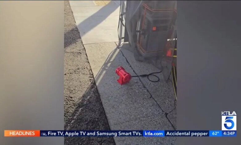 A red siren connected by a black cord, sitting on a concrete sidewalk next to the road.