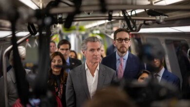 California Governor Gavin Newsom on a train, surrounded by a crowd and cameras.