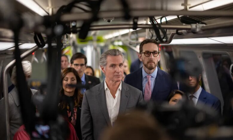 California Governor Gavin Newsom on a train, surrounded by a crowd and cameras.