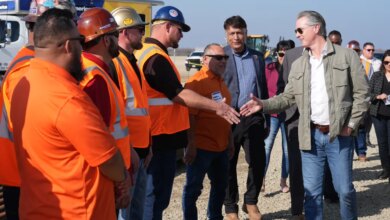California Gov. Gavin Newsom shaking hands with an Iron Workers Local 155 worker as Ian Choudri, CEO for the California High-Speed Rail Authority, watches.