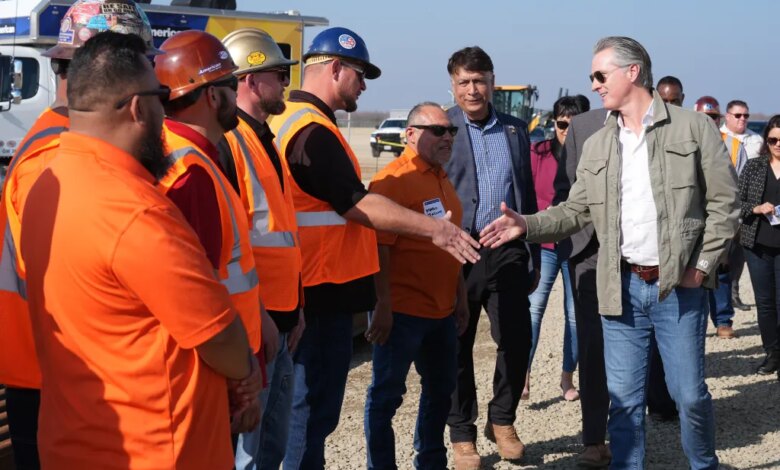 California Gov. Gavin Newsom shaking hands with an Iron Workers Local 155 worker as Ian Choudri, CEO for the California High-Speed Rail Authority, watches.