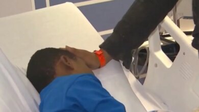 A person in a black sleeve touching the forehead of a child lying in a hospital bed.