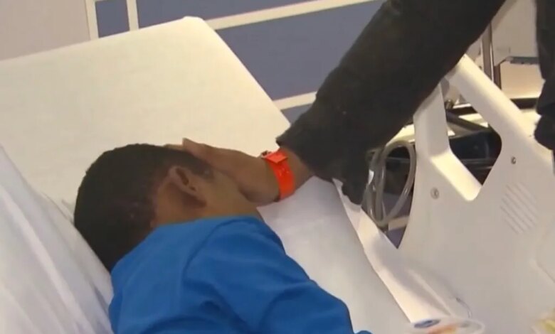 A person in a black sleeve touching the forehead of a child lying in a hospital bed.