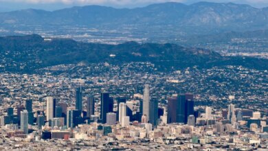 Aerial view of downtown Los Angeles with the Hollywood sign on a distant mountain and additional mountains in the background.