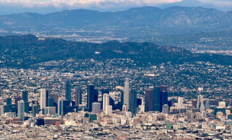 Aerial view of downtown Los Angeles with the Hollywood sign on a distant mountain and additional mountains in the background.