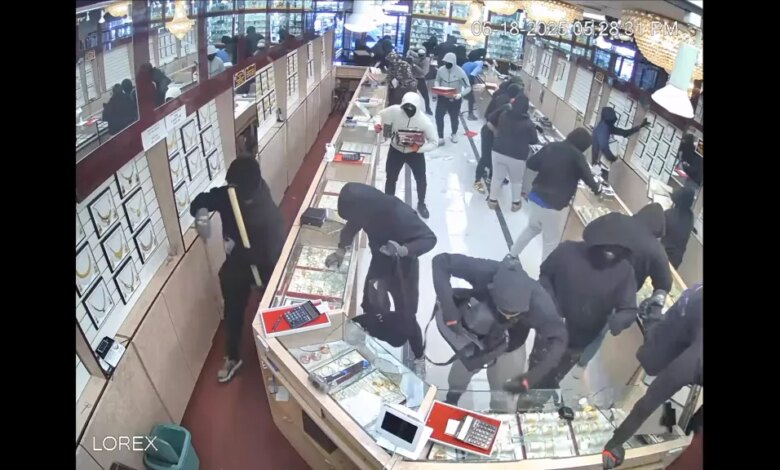 Multiple masked people smash glass display cases in a jewelry store during a robbery.