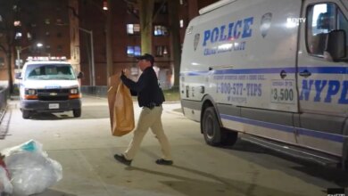 A police officer carrying a large brown bag walks past a police crime scene unit van at night.