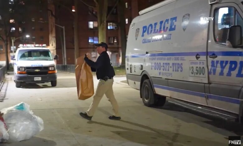 A police officer carrying a large brown bag walks past a police crime scene unit van at night.