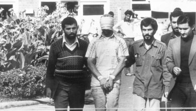 A blindfolded and bound hostage is led by Iranian students in front of a building.