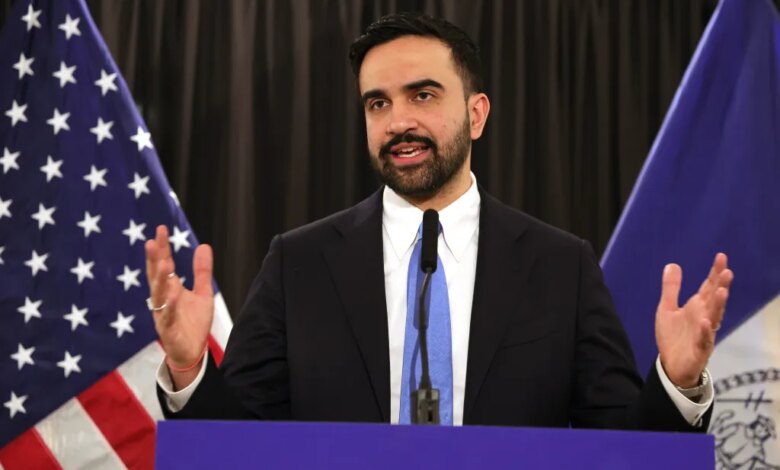 Mayor Zohran Mamdani speaking at a press conference with American and New York flags in the background.