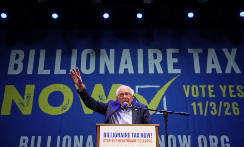Senator Bernie Sanders speaks at a podium in front of a blue banner that reads "Billionaire Tax Now!" and "Vote Yes 11/3/26".