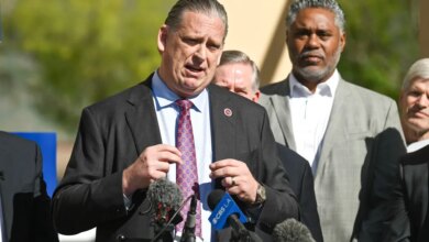 Sen. Tony Strickland speaking at a press conference with two microphones in front of him and other men behind him.