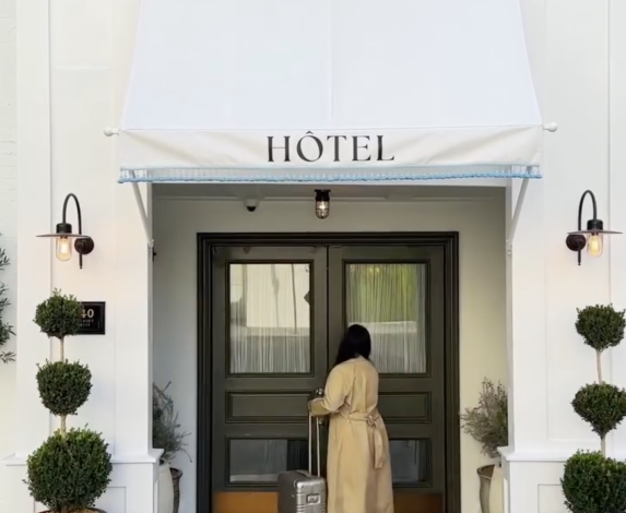A person with a suitcase approaches the entrance of a building with an awning that says "HÔTEL".