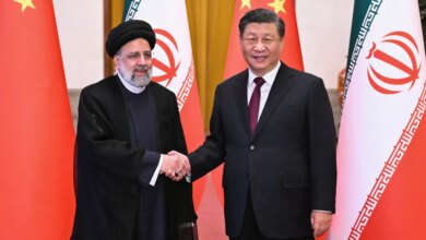 Iranian President Ebrahim Raisi and Chinese President Xi Jinping shake hands in front of their national flags.