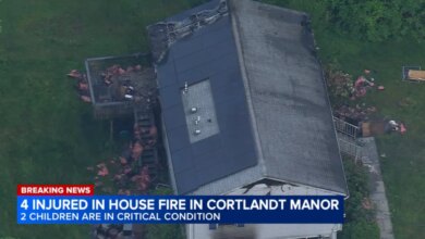 Aerial view of a house with extensive fire damage to the roof and a news overlay stating "4 INJURED IN HOUSE FIRE IN CORTLANDT MANOR, 2 CHILDREN ARE IN CRITICAL CONDITION."