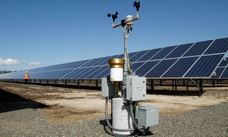 A weather station stands in front of solar panels at a solar energy site.
