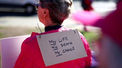 A demonstrator wears a sign that reads "My Life, My Death, My Choice"