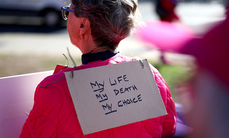 A demonstrator wears a sign that reads "My Life, My Death, My Choice"