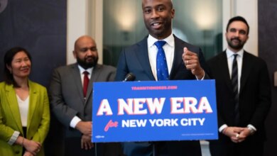 Kamar Samuels speaking at a podium with "A NEW ERA for NEW YORK CITY" on it, with three people standing behind him.