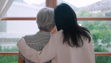 A daughter hugging her mother as they look out a window on a rainy day.