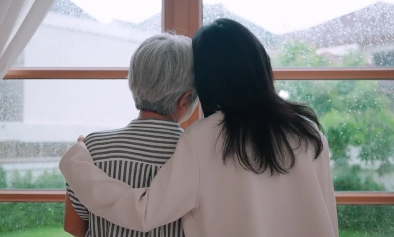 A daughter hugging her mother as they look out a window on a rainy day.