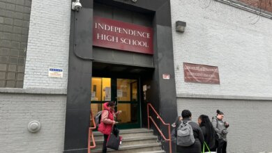 Students stand on the steps and sidewalk outside Independence High School, where a video surveillance notice is posted on the wall.