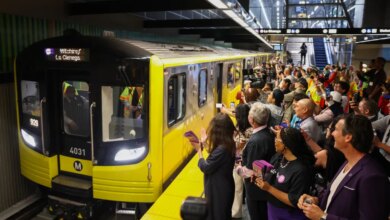 A new Metro D Line subway train arrives at the Wilshire/Fairfax station as people on the platform cheer and take photos.