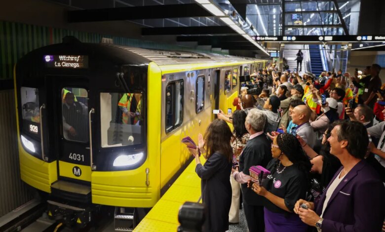 A new Metro D Line subway train arrives at the Wilshire/Fairfax station as people on the platform cheer and take photos.