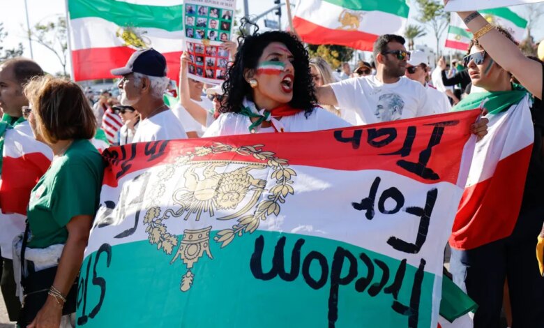 A woman with face paint in the colors of the Iranian flag holds a banner that reads "Freedom for Iran" while participating in a protest.