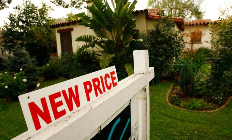 A "NEW PRICE" real estate sign in front of a stucco house with a tile roof and green landscaping.