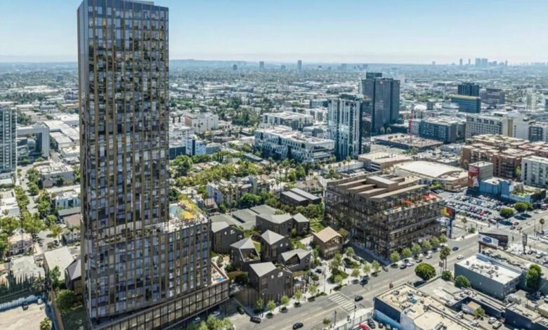 Aerial view of a mixed-use development with a tall skyscraper, mid-rise buildings, and smaller structures alongside a street in a city.