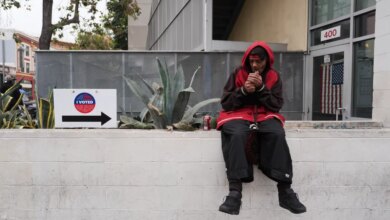 A man in a red hoodie lighting a cigarette outside a voting center with an "I Voted" sign nearby.