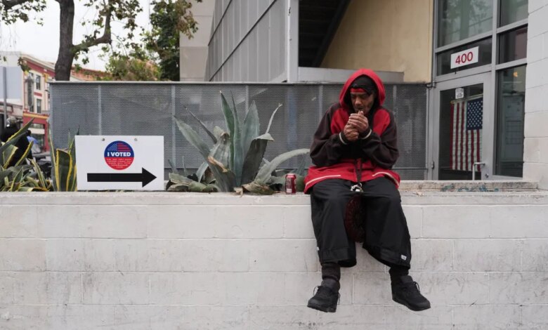 A man in a red hoodie lighting a cigarette outside a voting center with an "I Voted" sign nearby.