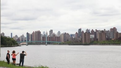 Three people standing by the water, looking at the city skyline with a bridge in the distance.