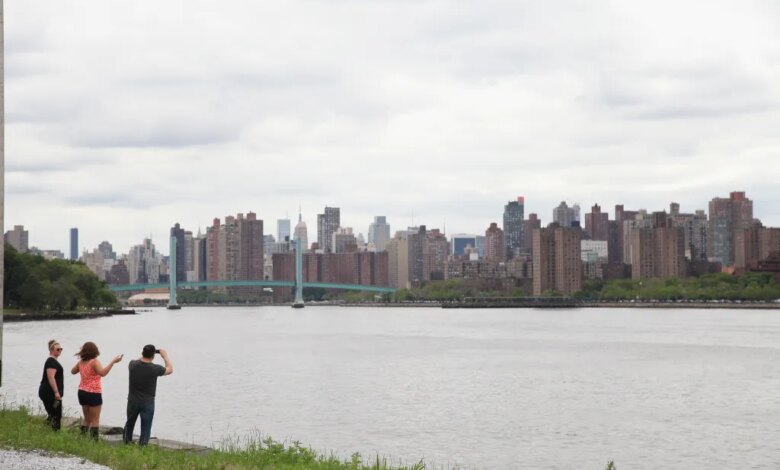 Three people standing by the water, looking at the city skyline with a bridge in the distance.