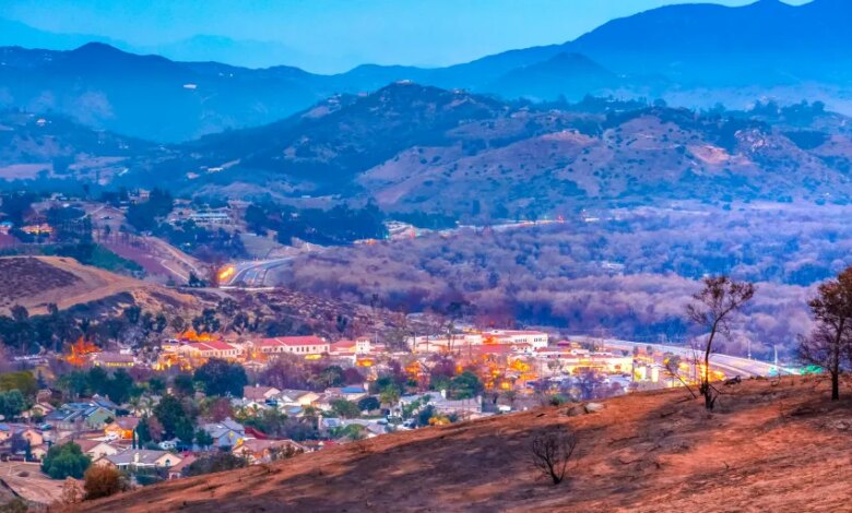 View of homes in Fallbrook, California, near hills destroyed by the Lilac Fire, with burnt ground and trees.