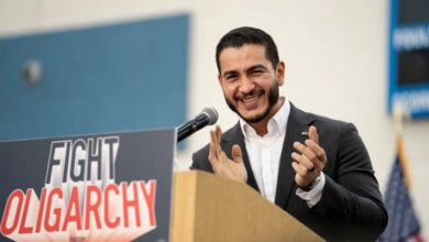 Abdul El-Sayed speaking from a podium with a "FIGHT OLIGARCHY" sign.