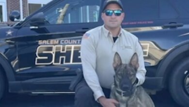 Sgt. Cody Henderson kneeling beside K9 Rip, with a Salem County Sheriff vehicle and courthouse in the background.