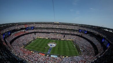 A general view of a soccer stadium packed with fans, with a large "FIFA World Cup 2026 THE FINAL" logo on the field and four F-16 fighter jets flying overhead.
