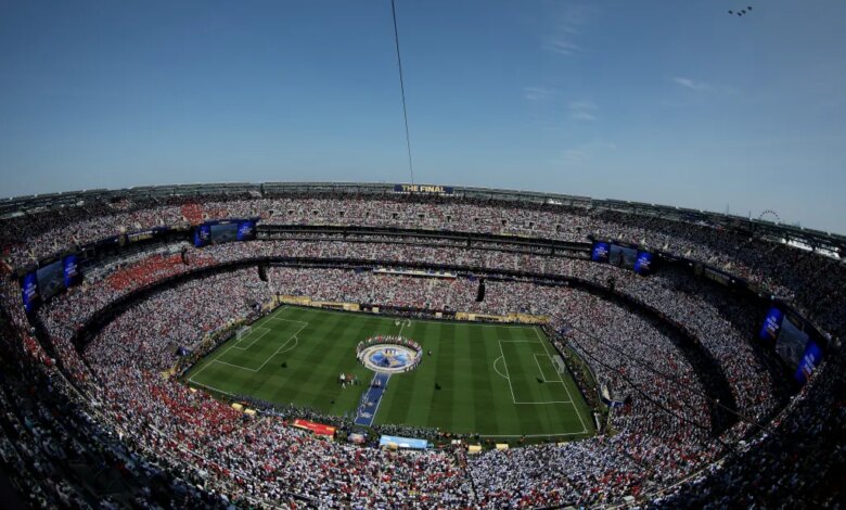 A general view of a soccer stadium packed with fans, with a large "FIFA World Cup 2026 THE FINAL" logo on the field and four F-16 fighter jets flying overhead.