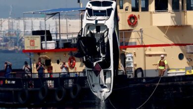 An overturned bowrider motorboat is lifted from the water by a crane vessel.