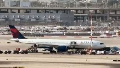A Delta Air Lines passenger plane parked at an airport tarmac, surrounded by service vehicles.