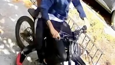Surveillance footage of two suspects riding a motorized bike on a sidewalk, sought in connection with a robbery.